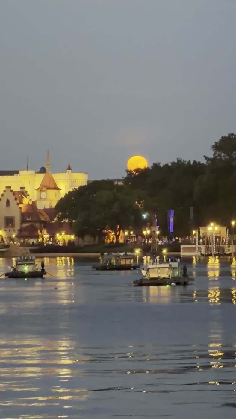 A golden moon rising over a lagoon as boats drift by at dusk