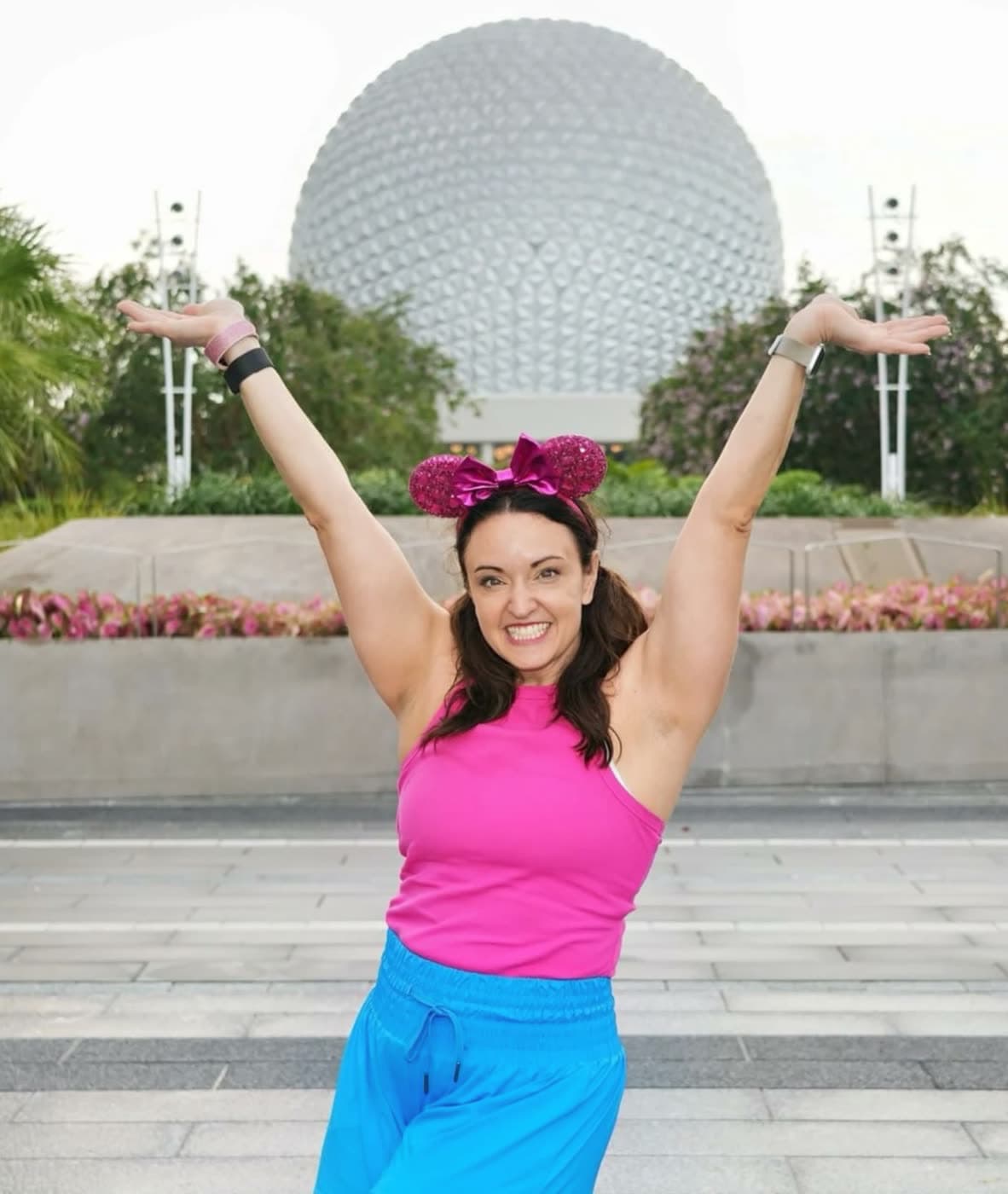 Nikki in sparkly pink ears, arms raised in front of a geodesic sphere