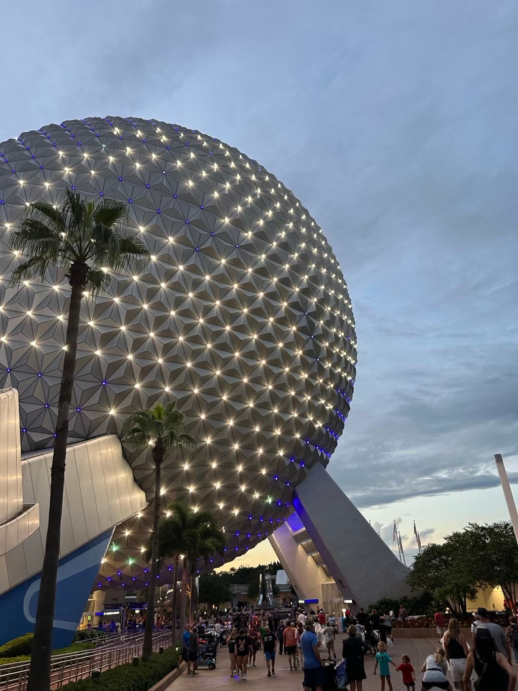 A geodesic sphere lit up at dusk behind palm trees