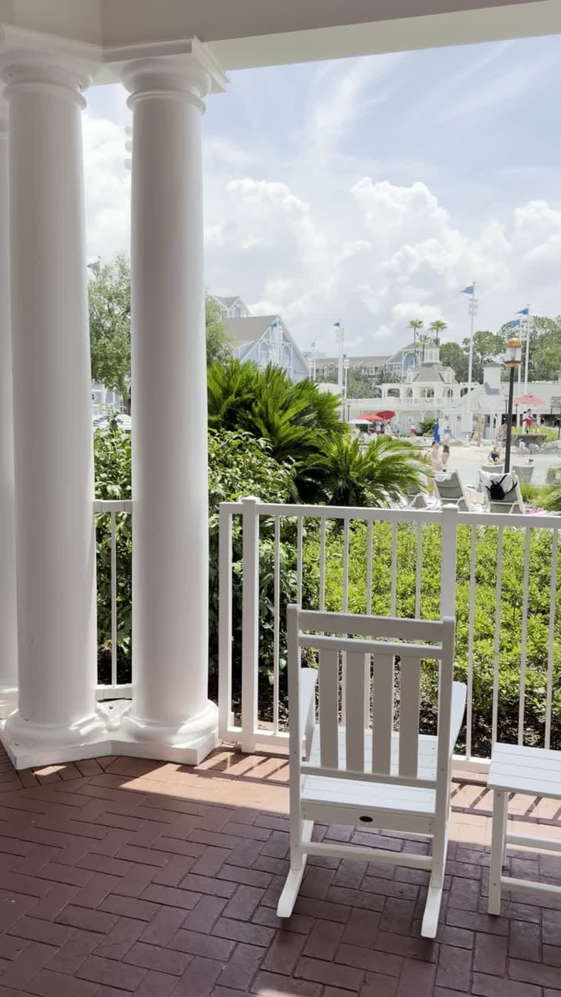White rocking chairs on a columned resort porch overlooking palm trees